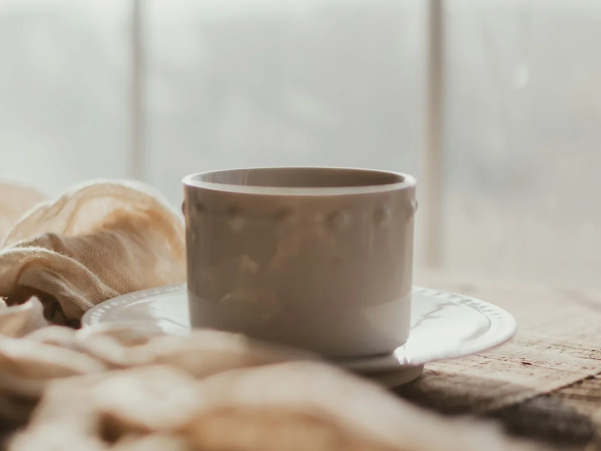 Una taza junto a una ventana con luz natural y una tela sobre la mesa